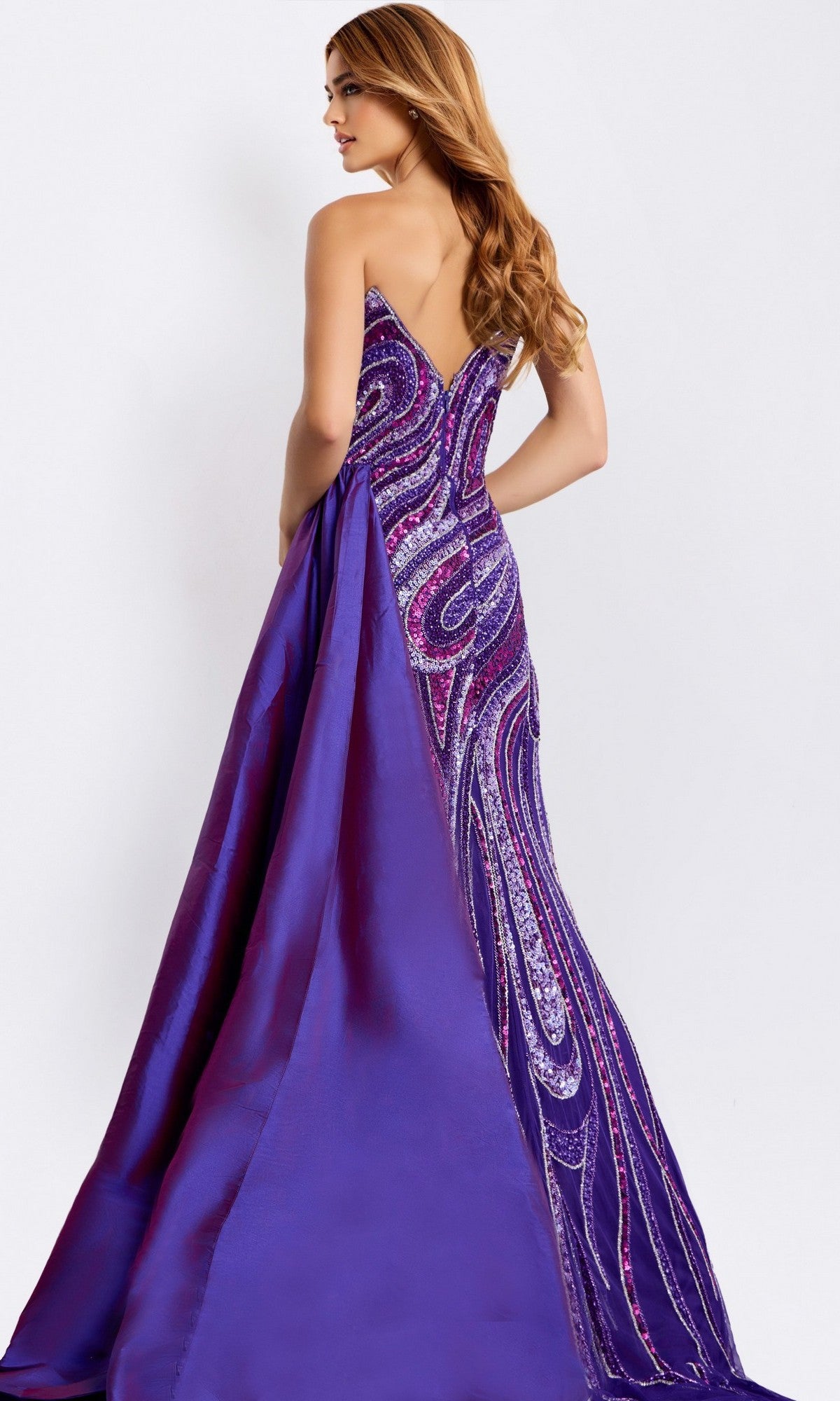 A woman models the Jovani 49226 long prom dress—purple, strapless, with a sweeping train and swirling sequin patterns—standing with her back to the camera.